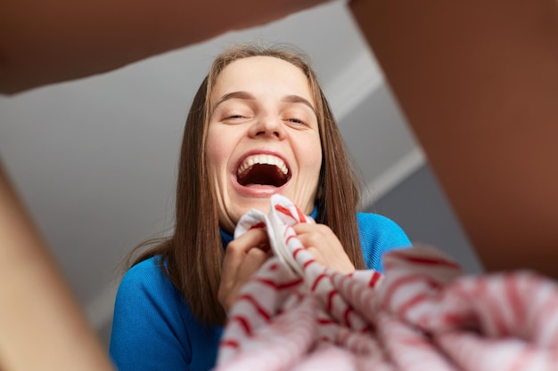 Quick purchases in online store Satisfied cheerful Caucasian brown haired woman opening carton box and taking clothing from container rejoicing smiling happily