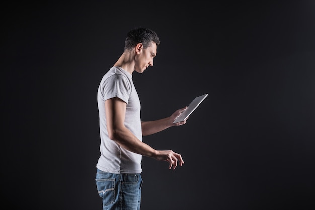 Quick typing. Nice smart adult man holding a tablet and looking at the text on its screen while typing it