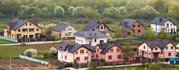 Тихий жилой пригородный район. Улица с новыми современными уютными кирпичными коттеджами с дворами и цветущими садами на фоне красивого зеленого леса. Инвестиции в недвижимость.