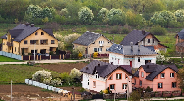 Quiet residential suburban area. Street with new modern comfortable brick cottages with yards and blooming gardens on beautiful green forest. Investments in real estate concept.