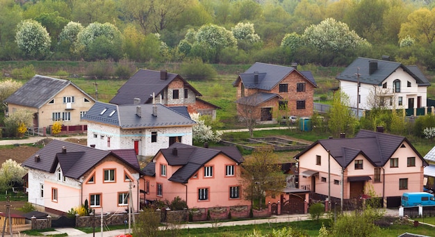 Тихий жилой пригородный район. Улица с новыми современными уютными кирпичными коттеджами с дворами и цветущими садами на сцене красивого зеленого леса. Инвестиции в недвижимость.