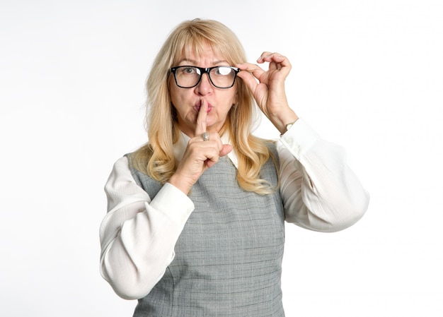 Quiet! Standing woman in glasses shows a gesture of silence on a light background. Keep your finger near the lips.