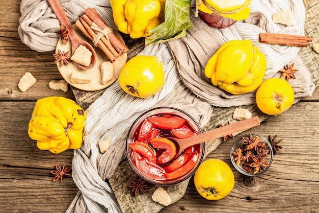 Quince jam or confiture brewed with brown sugar. Ripe whole fruits, sweet dessert, fragrant spices. Trendy wooden stand, old boards background, top view