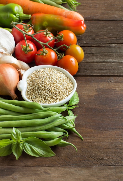 Quinoa in een kom en verse groenten op een bruine houten lijst sluiten omhoog