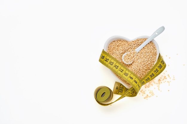 Quinoa korrels met meetlint in kom van de vorm van hart geïsoleerd op een witte tafel, bovenaanzicht. Concept van keto-dieet en goede voeding.