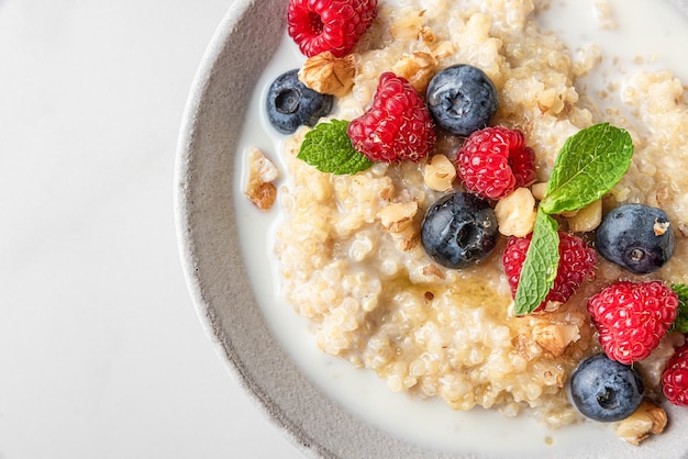 Quinoa pap met verse bosbessen, frambozen, walnoten, honing en munt in een schaal op een witte achtergrond