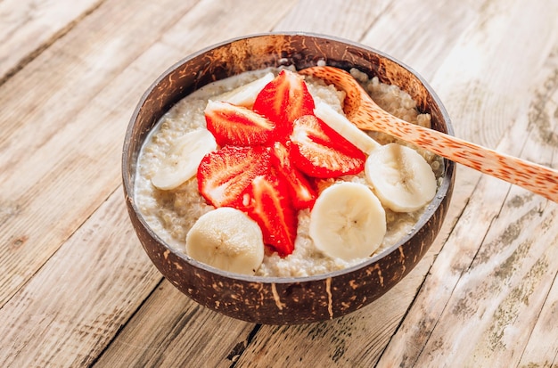 Quinoa porridge with coconut milk and fresh strawberries in a coconut bowl wooden rustic background Healthy Lactose and Gluten Free Breakfast Top view