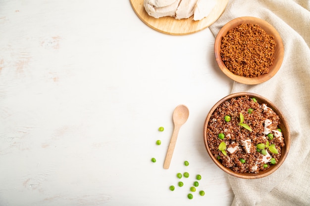 Porridge di quinoa con piselli e pollo in ciotola di legno su un fondo di legno bianco.