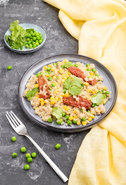 Quinoa porridge with green pea, corn and dried tomatoes on ceramic plate on a gray concrete background. Side view, close up.