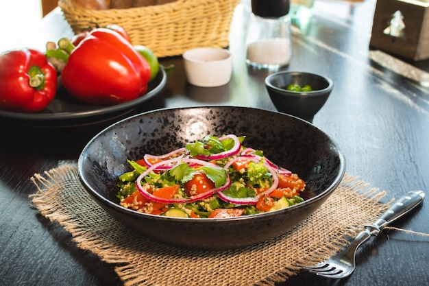 Quinoa salad with tomatoes, avocado, paprika and parsley on black stone plate.