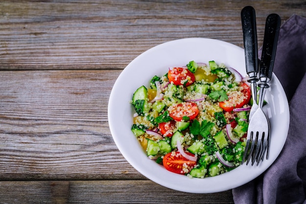 Quinoa Tabbouleh salad bowl with cucumbers tomatoes red onions and parsley on wooden background