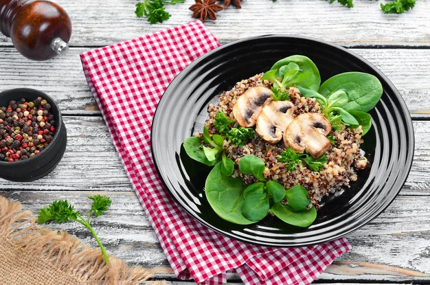 Quinoa with spinach and mushrooms In a black plate on a wooden background Top view Free space for your text Flat lay