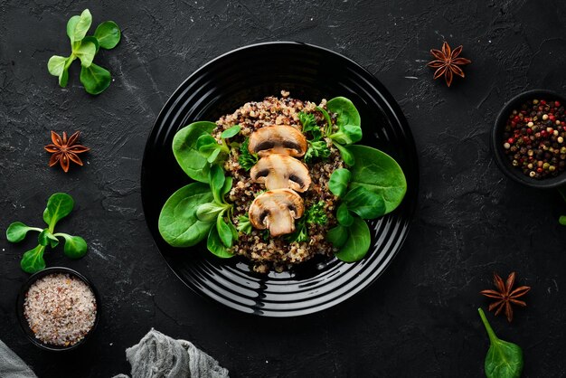 Quinoa with spinach and mushrooms In a black plate on a wooden background Top view Free space for your text Flat lay