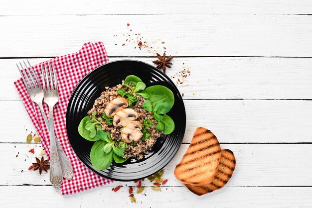 Quinoa with spinach and mushrooms In a black plate on a wooden background Top view Free space for your text Flat lay