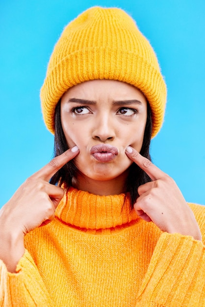 Quirky goofy and young female in a studio with a comic funny and crazy face expression Gen z silly and beautiful woman model from Puerto Rico touching her cheeks isolated by a blue background