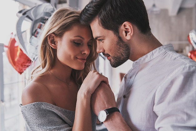 Quite moments together. Beautiful young couple holding hands while standing in the bedroom full of balloons