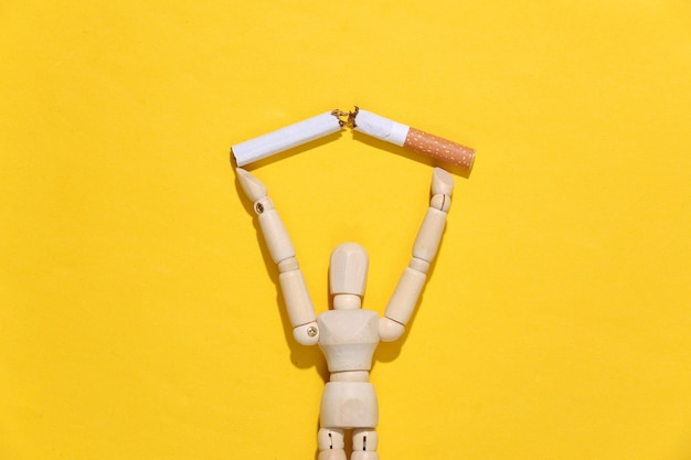 Quitting smoking. Wooden puppet figurine holding broken cigarette on yellow background