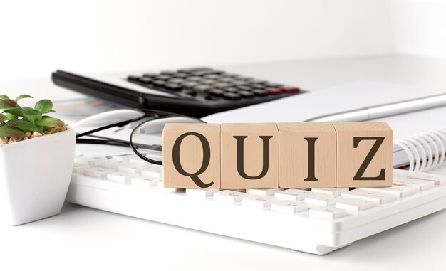 QUIZ written on a wooden cube on keyboard with office tools