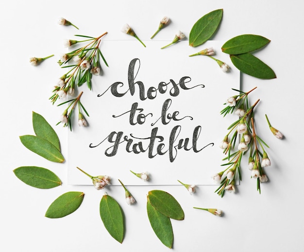 Quote Choose to be grateful written on paper with leaves and flowers on white background Top view