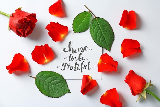 Quote Choose to be grateful written on paper with petals and leaves on white background Top view