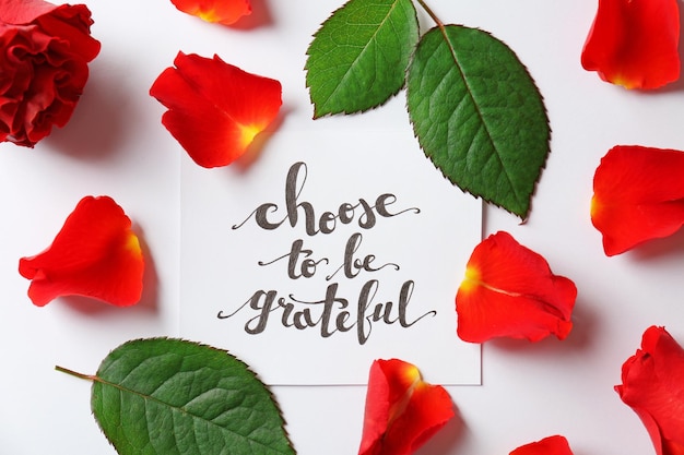 Quote Choose to be grateful written on paper with petals and leaves on white background Top view