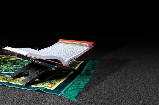 Photo quran open on a wooden placemat on a prayer rug