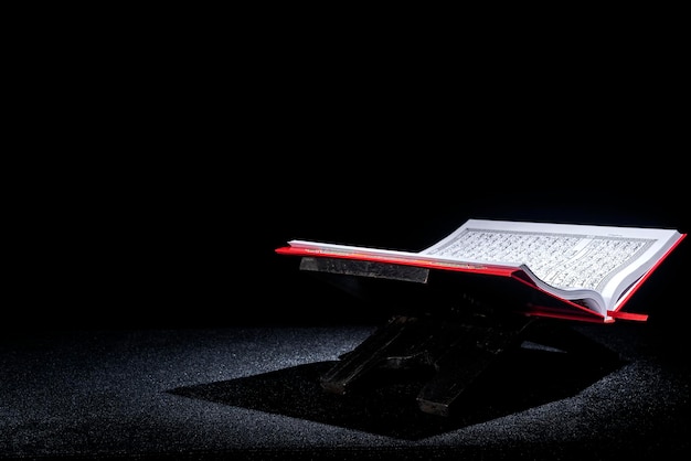 Quran open on a wooden placemat with dark background