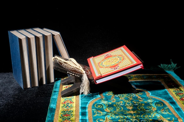 Quran on a wooden placemat in prayer rug with prayer beads on dark background