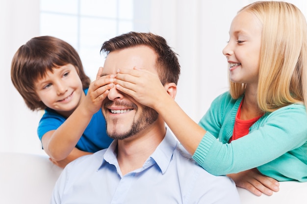 Raad eens wie? Twee speelse kinderen die de ogen van hun vrolijke vader bedekken en glimlachen