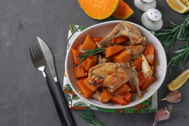 Rabbit meat with pumpkin and garlic in a light plate on dark gray background