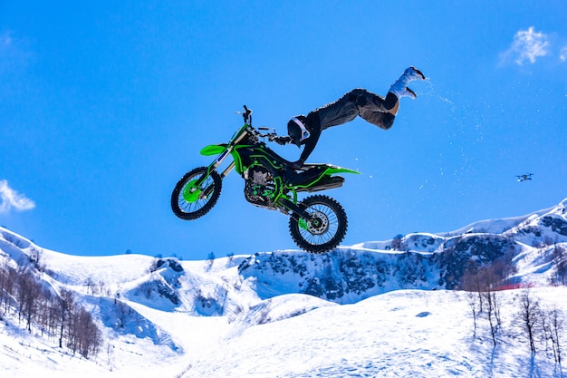 Racer on a motorcycle in flight, jumps and takes off on a springboard against the snowy mountains