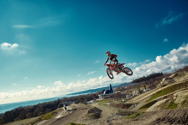 Photo racer on mountain bike participates in motocross race takes off and jumps on springboard against the