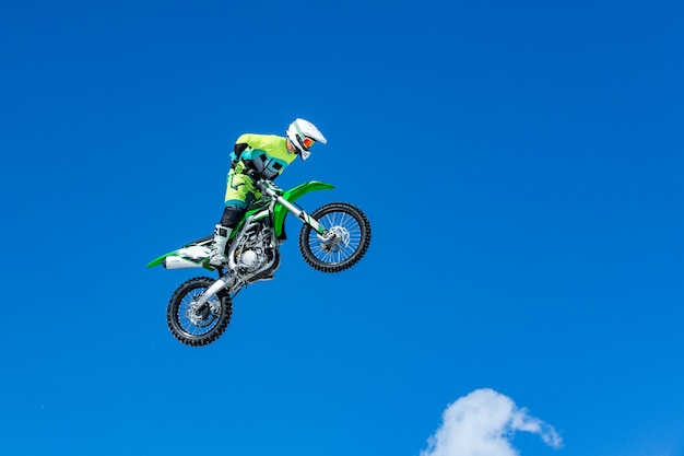 Гонщик на мотоцикле в полете, прыгает и взлетает на трамплине на фоне голубого неба
