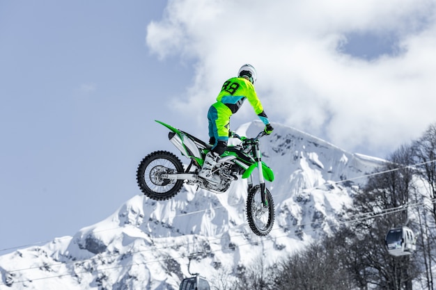 Racer op een motorfiets tijdens de vlucht, springt en vertrekt op een springplank tegen de besneeuwde bergen