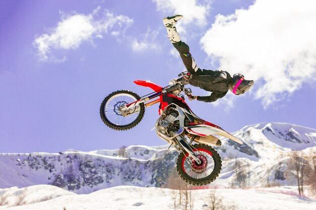 Racer op een motorfiets tijdens de vlucht, springt en vertrekt op een springplank tegen de besneeuwde bergen