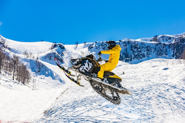 Racer on a snowcat in flight, jumps and takes off on a springboard against the snowy mountains