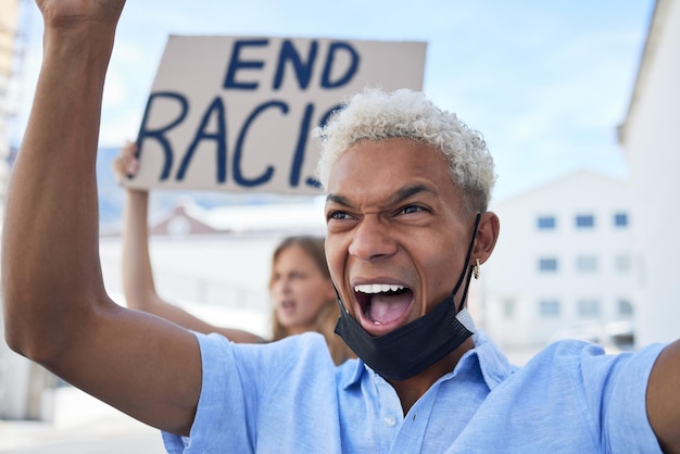 Протест против расизма и человека с картонным плакатом и криком на улице в маске во время пандемии Разочарованный правозащитник, протестующий со знаком равенства или справедливости в городе