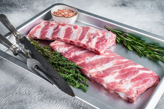 Rack of Raw pork spare ribs in kitchen oven tray with herbs. White background. Top view.