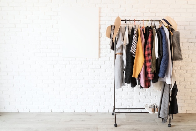 Photo rack with colorful clothes on hangers and frame canvas for mock up over white brick wall. mock up design