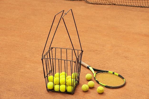 Racket and basket with balls on clay court