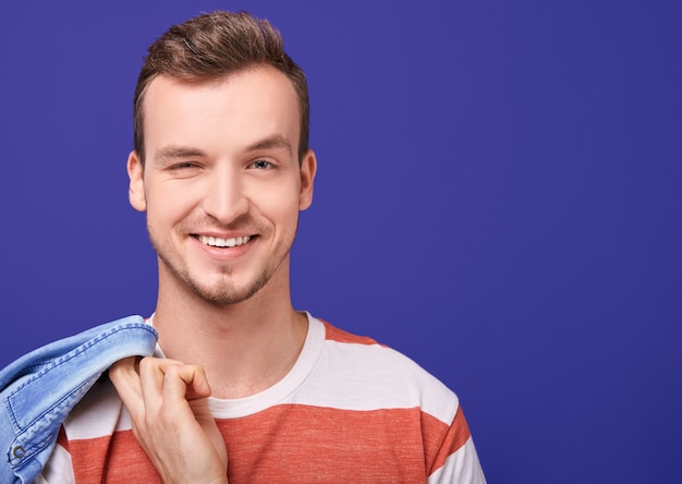 Radiant smiling beauty man in striped t-shirt looks straight and winks with one eye