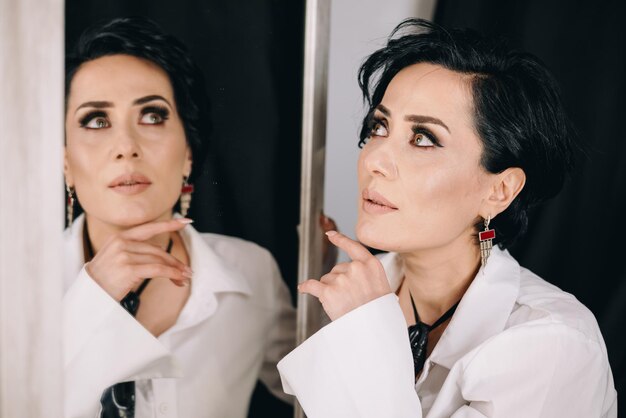 Radiant woman with brilliant eyes in white shirt posing with a mirror and examining her reflection