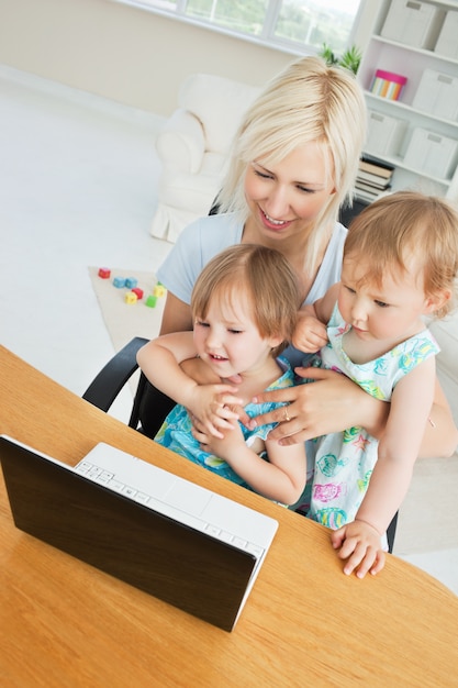 Radiant woman working with her children at laptop