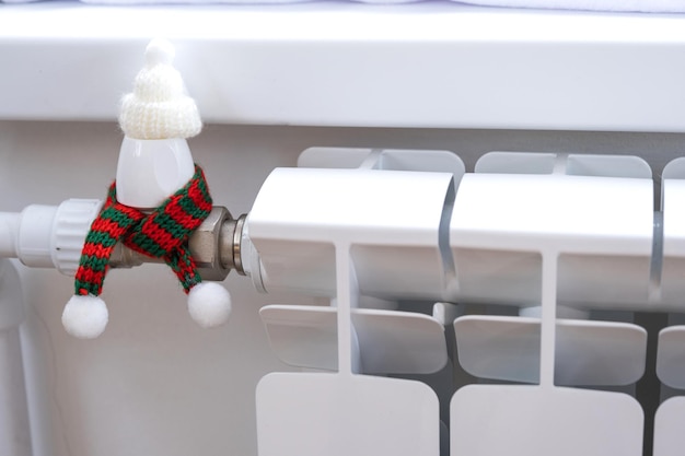 Radiator in huis is gewikkeld in een gebreide sjaal en een muts Warmte en comfort in huis isolatie winterklaar maken Feestelijk decor voor kerst en nieuwjaar Warmtegas besparen in een crisis