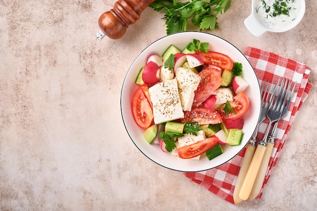 Radijs, komkommer, tomaat, peper en feta-kaas met kruiden, peper en olijfolie in witte kom op grijze leisteen, steen of betonnen ondergrond. Gezond voedselconcept. Bovenaanzicht.