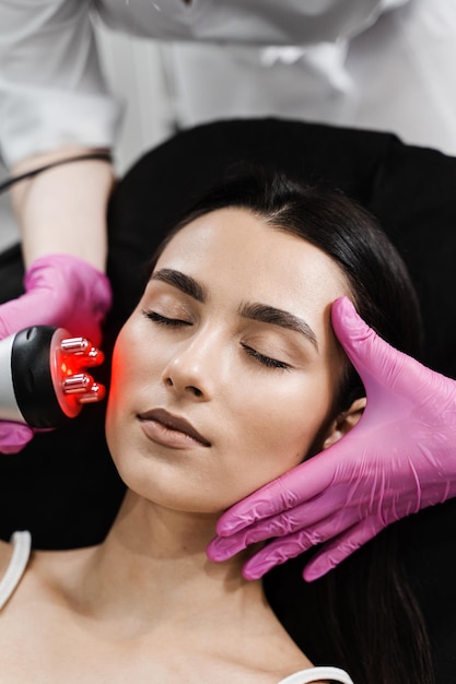 Radio frequency lifting with red light for young woman closeup Dermatologist is doing radio frequency RF skin tightening RF facelift firms and lifts sagging skin