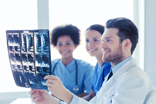 radiologie, chirurgie, gezondheidszorg, mensen en geneeskunde concept - groep gelukkige artsen kijken naar en bespreken röntgenbeeld van de wervelkolom in het ziekenhuis