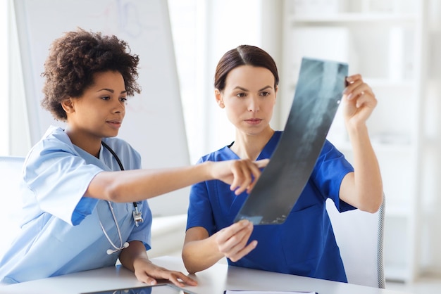 radiology, surgery, people and medicine concept - female doctors looking to and discussing x-ray image at hospital