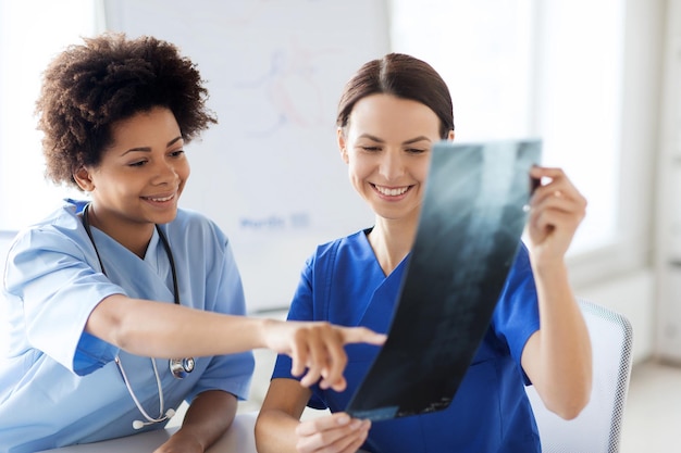 radiology, surgery, people and medicine concept - happy female doctors looking to and discussing x-ray image at hospital