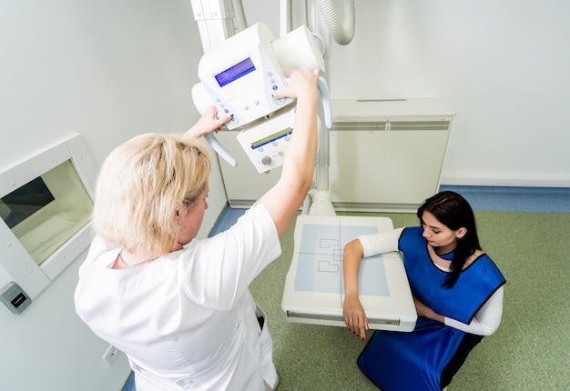 Radioloog en patiënt in een x-ray kamer. röntgenfoto van menselijke hand. klassiek röntgensysteem voor plafondmontage.